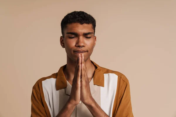 年轻英俊的非洲男子 紧闭双眼 双手交叉地做着祈祷手势 站在孤立的米黄色背景上 — 图库照片