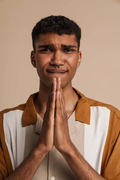 年轻英俊而紧张的非洲男人 紧闭双眼 双手交叉地做祷告动作 而站在孤立的米黄色背景上 — 图库照片