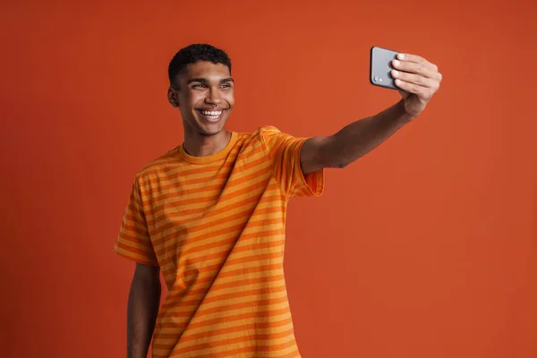 年轻英俊的微笑着的快乐的非洲男人 带着刺穿自己的手机 站在孤立的橙色背景上 — 图库照片