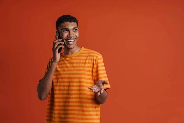 年轻英俊的快乐微笑的非洲男人 一边站在孤立的橙色背景上一边 一边打电话一边看一边穿孔 — 图库照片