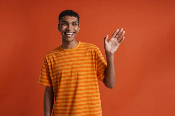 若いですハンサムな笑顔幸せなアフリカ人男でピアス手を振ってカメラを見て 隔離されたオレンジの背景の上に立っている間 — ストック写真
