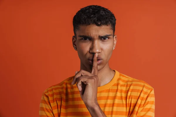 年轻英俊的皱眉的非洲男人 用手指捂住嘴唇 站在孤立的橙色背景上看着相机 表现出沉默的姿态 — 图库照片