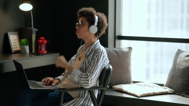 自宅でヘッドフォンでラップトップで働いている集中ヒスパニックの巻き毛の女性 — ストック動画