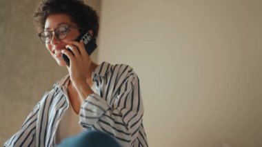 Pozitif İspanyol kıvırcık saçlı kadın telefonda evdeki yatakta konuşuyor.