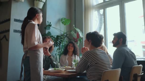 ウエイトレスはカフェで誕生日を祝う多国籍の友人に食べ物について話します パーティーのコンセプト — ストック動画