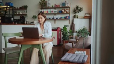 Beyaz tişörtlü konsantre olmuş yaşlı kadın kafeteryada dizüstü bilgisayar arıyor ve çalışıyor.