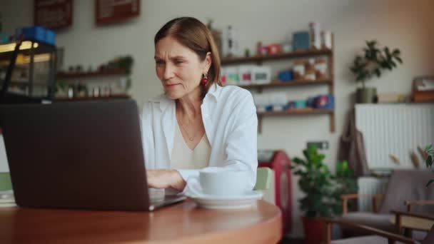 全神贯注的老年妇女穿着白衬衫在咖啡店的笔记本电脑上远程工作 — 图库视频影像