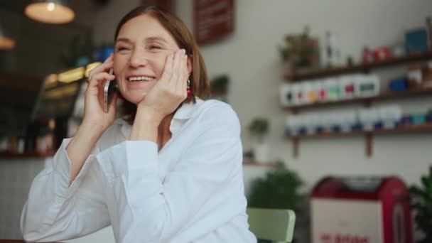 Счастливая Пожилая Женщина Белой Рубашке Разговаривает Мобильному Телефону Кафе — стоковое видео
