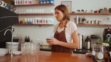 Neşeli yaşlı bayan barmen masayı temizler ve barın arkasındaki kameraya bakar.