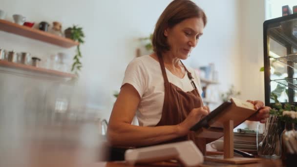 笑顔高齢女性Barista入力注文上のタブレット後ろカウンターでカフェ — ストック動画