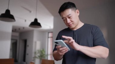 Evdeki mutfakta cep telefonuyla mesaj atan düşünceli Asyalı adam.