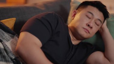 Yorgun Asyalı adam TV izliyor ve evdeki kanepede uyuyor.