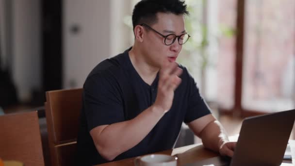 ハンサムなアジアの男で眼鏡でビデオ通話でラップトップ上の家 — ストック動画