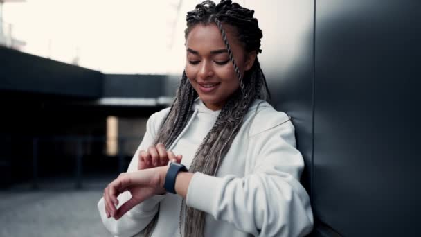 トレーニングの後 腕時計の外にメッセージ編組ピグテールを持つ幸せなアフリカの女性 スポーツ活動 アクティブなライフスタイル — ストック動画