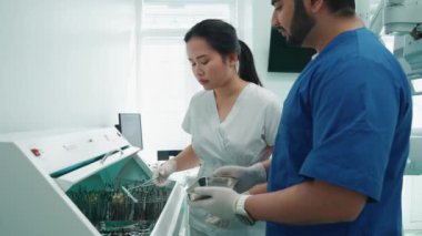 Kendine güvenen çok uluslu iş arkadaşları dişçiler kurutucudan tepsiye steril aletler koydular.