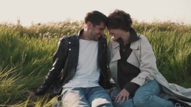 Gülen çift deniz kenarında piknik battaniyesinde otururken konuşuyor.