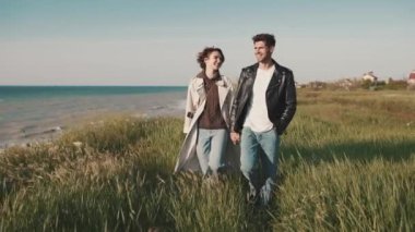 Gülümseyen çift deniz kenarında yürürken konuşuyor ve el ele tutuşuyorlar.