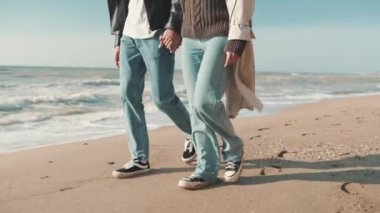 Deniz kıyısında yürürken el ele tutuşan şık bir çift
