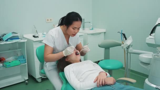 ハンサムなアジアの女性歯科医は病院で鏡で患者の口腔をチェックします 医者の予約 — ストック動画