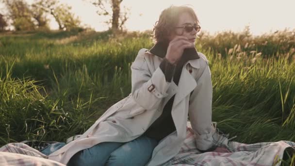 Hübsches Mädchen Brille Und Beigem Trenchcoat Sitzt Auf Picknickdecke Auf — Stockvideo
