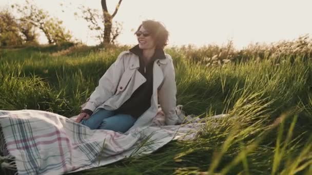 Cheerful Girl Glasses Beige Trench Coat Sitting Picnic Blanket Green — Stock Video
