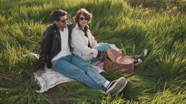 Gün Batımında Yeşil Çimlerde Piknik Battaniyesinde Oturan Gözlüklü Yakışıklı Çift — Stok video