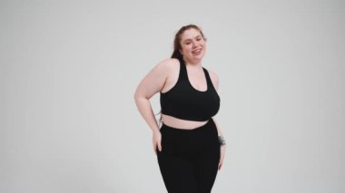 Yakışıklı, kızıl saçlı, siyah eşofmanlı bir kadın. Stüdyoda gri arka planda.