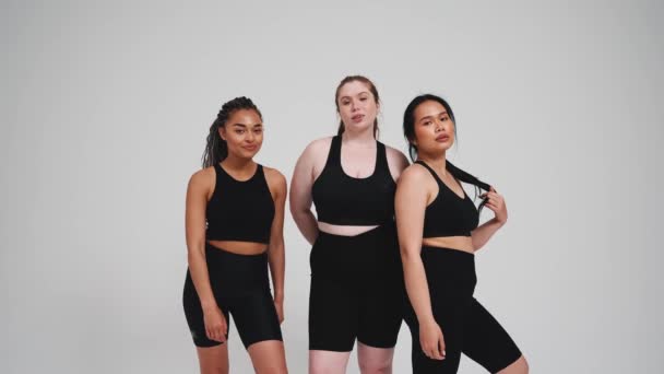 三个身穿黑色运动服的漂亮的跨国女孩在工作室里拍摄灰色背景的镜头 — 图库视频影像