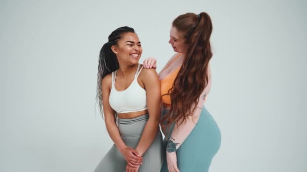 Дві Веселі Багатонаціональні Дівчата Спортивному Одязі Позують Камеру Сірому Фоні — стокове відео