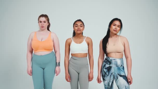 Trzy Piękne Wielonarodowe Kobiety Odzieży Sportowej Patrzące Kamerę Szarym Tle — Wideo stockowe