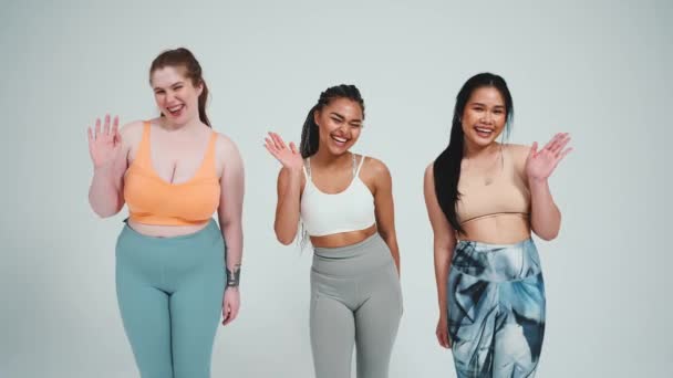 Tre Smukke Multietniske Kvinder Sportstøj Vinke Hænder Kameraet Mod Grå – Stock-video