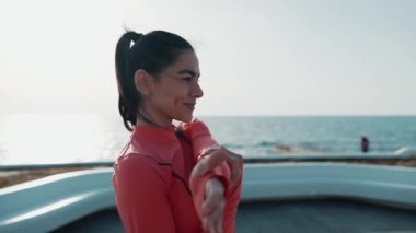 Gülümseyen esmer kadın, şafak vakti deniz kenarında ellerini uzatıyor.