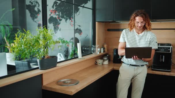 办公室厨房的笔记本电脑上 一个戴着眼镜 友善的卷发男人在工作 — 图库视频影像
