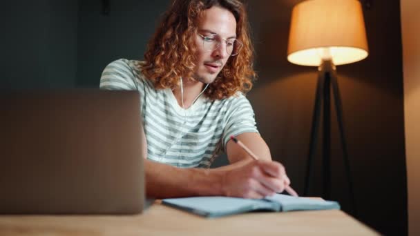 Concentrated Young Curly Long Haired Man Eyeglasses Writing Notepad Laptop — Stock Video