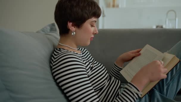 Mujer Joven Concentrada Con Piercings Leyendo Libro Sofá Casa — Vídeos de Stock