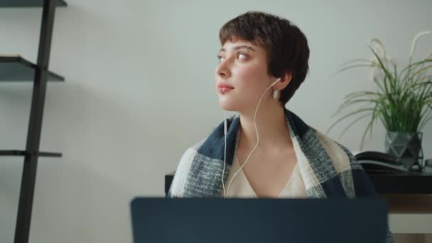 家でヘッドフォンでノートパソコンで作業毛布で覆われたピアスとハンサムな女性 — ストック動画