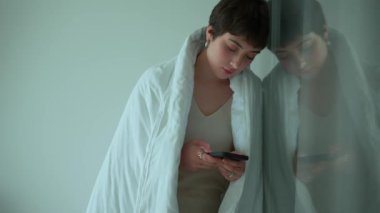 Piercingli depresif bir kadın. Battaniyeyle kaplanmış. Cep telefonuyla mesaj yazıyor.