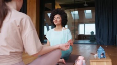Kadın antrenör ve güzel Afrikalı kadın yoga minderinde tütsüyle meditasyon yapıyorlar.