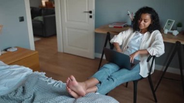 Güzel kıvırcık Afrikalı kadın laptopta evden çalışıyor. Uzak çalışma