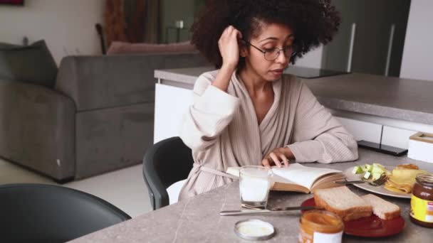Mulher Africana Meditativa Óculos Housecoat Livro Leitura Enquanto Toma Café — Vídeo de Stock
