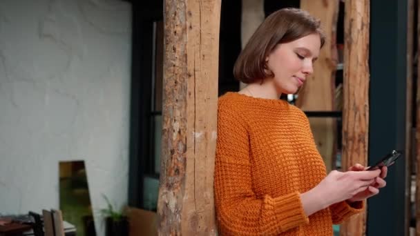 Mujer Sonriente Diseñadora Usando Suéter Naranja Enviando Mensajes Texto Teléfono — Vídeos de Stock