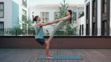 Funny couple of athletes doing yoga exercise on hotel balcony