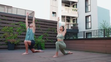 Happy couple of athletes doing yoga exercises and stretching upward on hotel balcony