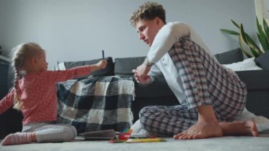 Şirin kıvırcık saçlı, sarışın baba-kız resimlerini boyama kitabında çiziyor ve evde yerde konuşuyor.