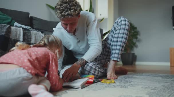 漂亮的父亲和女儿在家里的地板上画彩色书 — 图库视频影像
