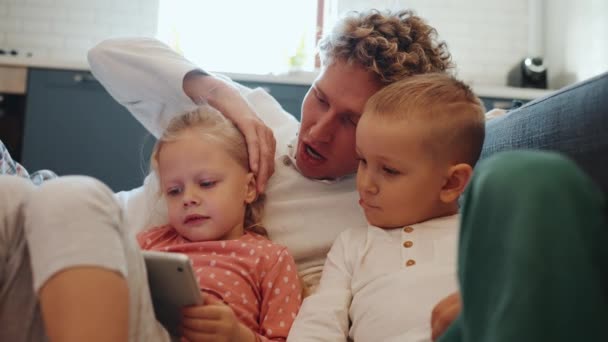 おかしいかわいい髪のブロンドの若い父親は子供と漫画を見て 自宅で床に抱きしめています — ストック動画