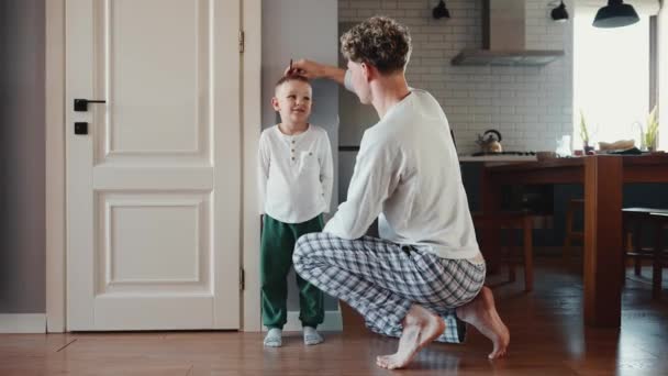 金髪の父親のバックビューは 壁の自宅で息子の身長を測定します — ストック動画