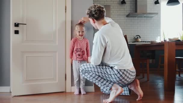 ハッピーブロンドの父親は壁の自宅で彼の娘の高さを測定し 次に息子が起きる — ストック動画