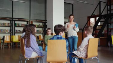 Kendine güveni tam bir öğretmen okuldaki sandalyelerde çember oluşturan çocuklarla konuşuyor.