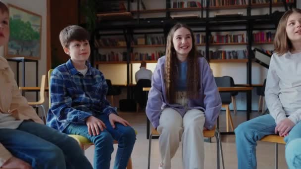 学校の図書館で円に座って話している陽気な子供たち — ストック動画